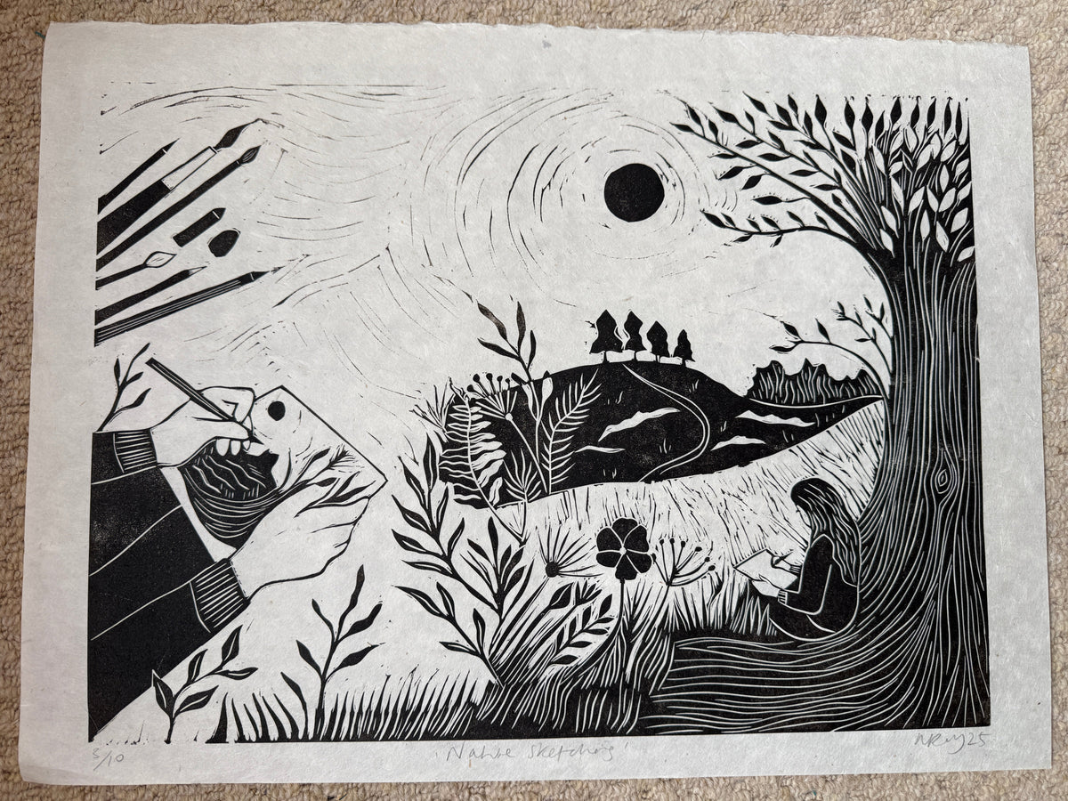 A black and white linocut or woodblock print on textured paper, depicting a hand holding a paintbrush and a fish, laid flat on a beige carpet background.